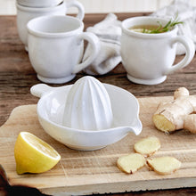 Load image into Gallery viewer, A white ceramic lemon juice squeezer with a cream-dipped base, placed on a wooden board with a lemon slice and pieces of ginger next to it.