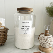 Load image into Gallery viewer, Glass jar of laundry powder with a white waterproof label with a wooden lid on a marble surface.