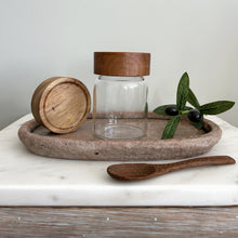 Load image into Gallery viewer, Glass jar with wooden lid on a stone tray with a wooden spoon and olive on a light background