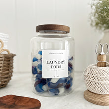 Load image into Gallery viewer, Jar of laundry pods with a white waterproof label and acacia lid on a white surface with decorative items.