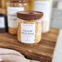 Load image into Gallery viewer, Clear glass jar with Acacia wood lid, labeled 'Yellow Split Peas', containing yellow split peas on a wooden surface.