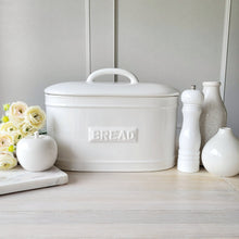 Load image into Gallery viewer, A white ceramic bread bin with 'BREAD' text embossed on the front, placed on a kitchen counter with decorative items and a vase of flowers beside it.