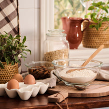 Load image into Gallery viewer, Kitchen counter with white ceramic egg tray , flour, and wooden spoon near a window with plants.
