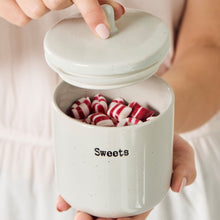 Load image into Gallery viewer, Person holding a small white ceramic container jar with a lid labelled 'Sweets' filled with candy.
