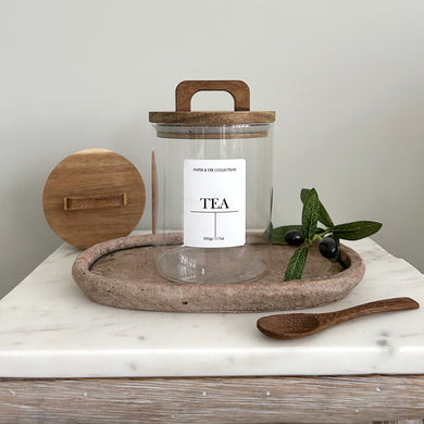 pantry Glass jar with white label tea with wooden acacia lid on a marble surface with olive branch and leaves.