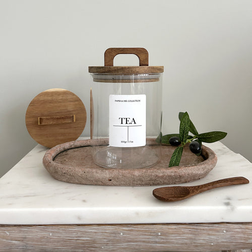 pantry Glass jar with white label tea with wooden acacia lid on a marble surface with olive branch and leaves.