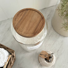 Load image into Gallery viewer, Glass jar with wooden lid on a marble surface with decorative items.
