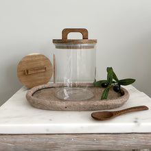 Load image into Gallery viewer, Clear glass jar with wooden lid and handle on a marble surface with olive branch
