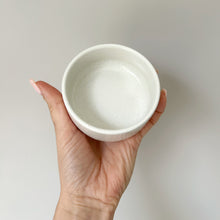 Load image into Gallery viewer, A hand holding a small, round, white ceramic tray against a plain, light gray background. Single white tray for a soap dispenser.
