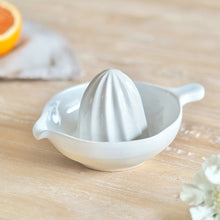 Load image into Gallery viewer, White cream ceramic juicer on a wooden surface with an orange and white flowers.
